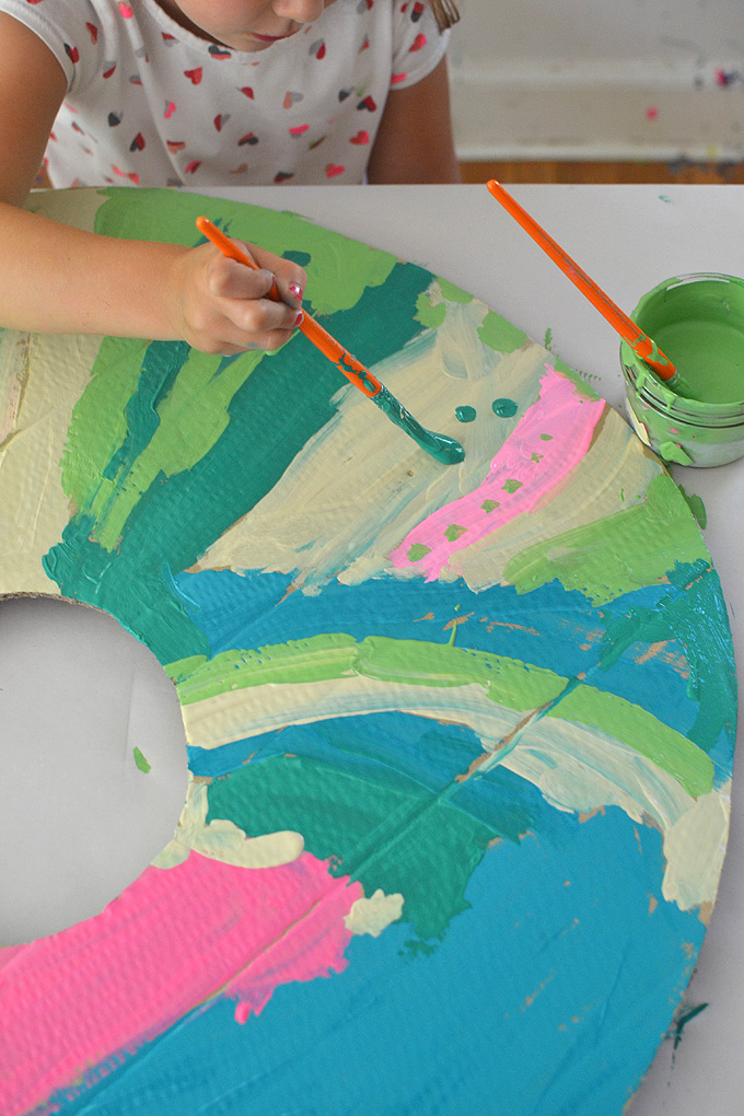 Mélanger les couleurs de peinture à l'aide de peintures à la détrempe pour peindre des beignets géants en carton.