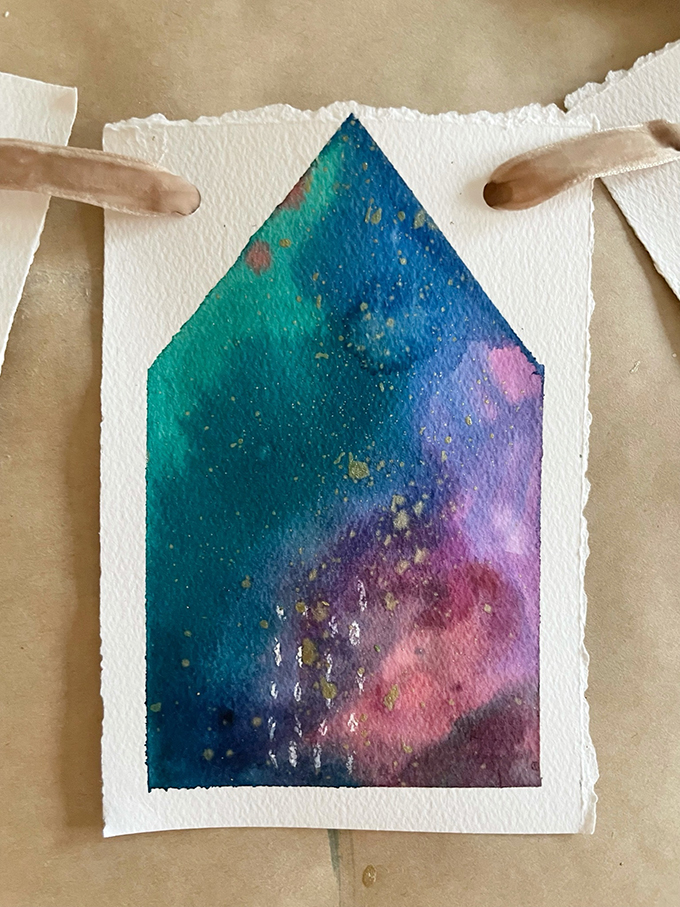 Fabriquez une guirlande de maison peinte en utilisant une technique d'aquarelle liquide et de ruban adhésif.