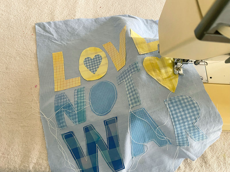 Coudre sur des lettres en tissu pour "L'amour pas la guerre" Bannière de bricolage faite avec de vieilles chemises.