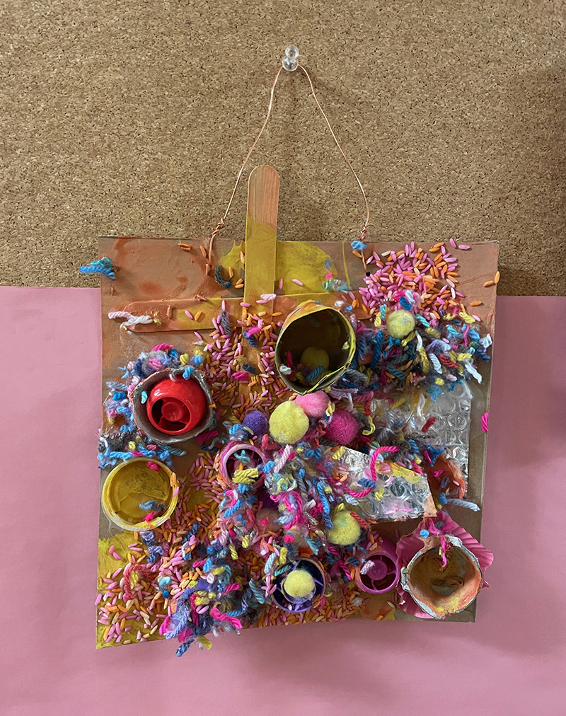 Un collage recyclé fini réalisé par un enfant d'âge préscolaire à l'aide de carton, de rouleaux de tp, de colle, de peinture et de fil