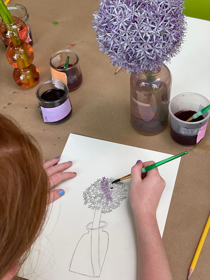 L'enfant dessine et peint une fleur dans un vase.