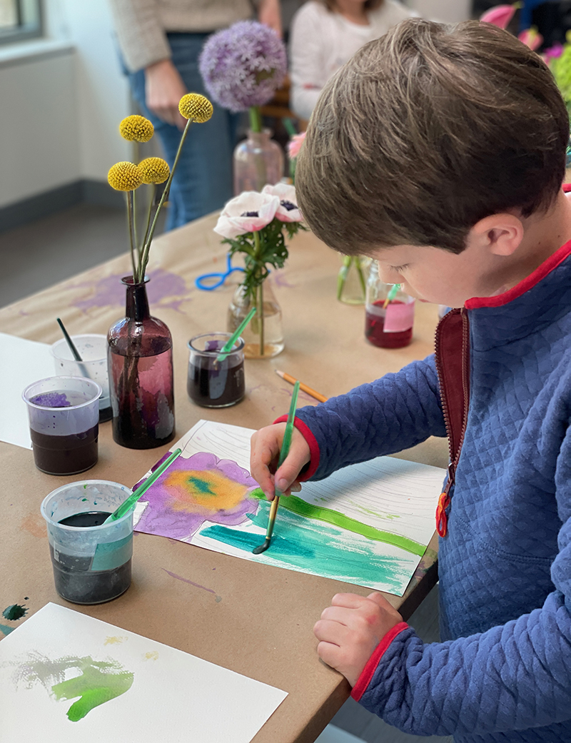 Le jeune garçon peint avec de l'aquarelle liquide à la table de nature morte de fleurs.