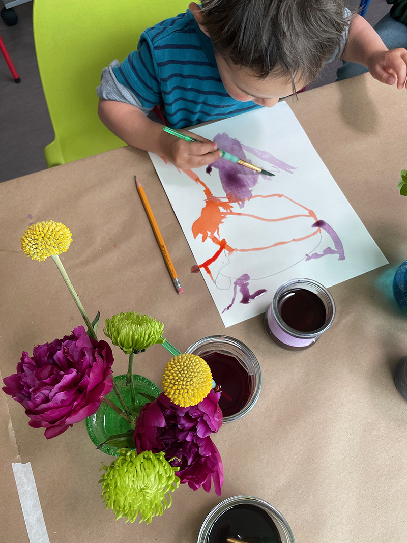 Toddler explore pour la première fois l'aquarelle liquide, inspirée de la table de fleurs des natures mortes.